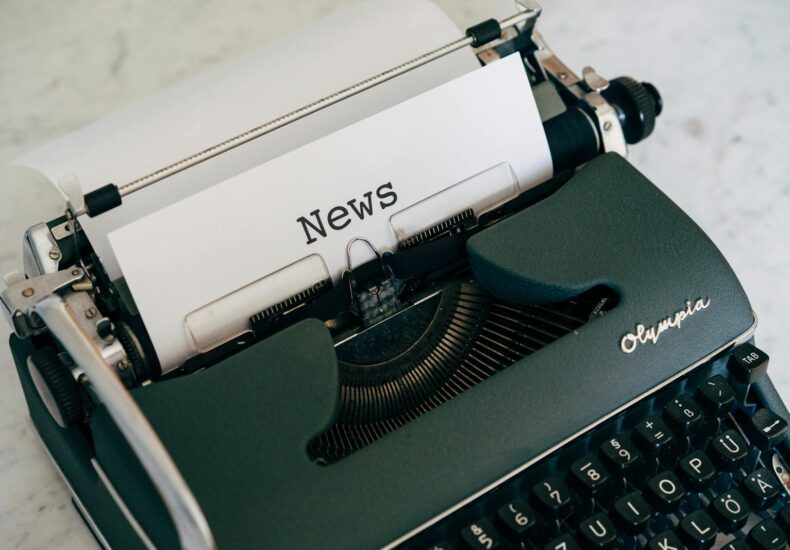 Close-up of an antique typewriter with 'News' on paper.