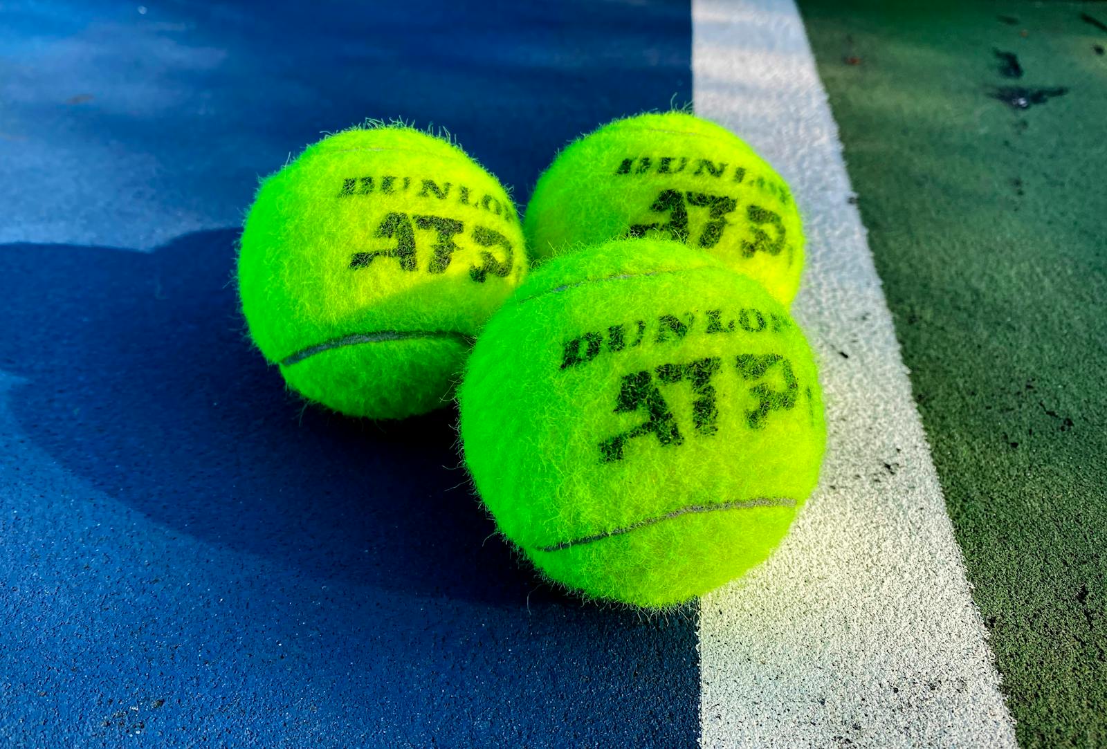 Vivid close-up of three Dunlop ATP tennis balls on a colorful outdoor court.